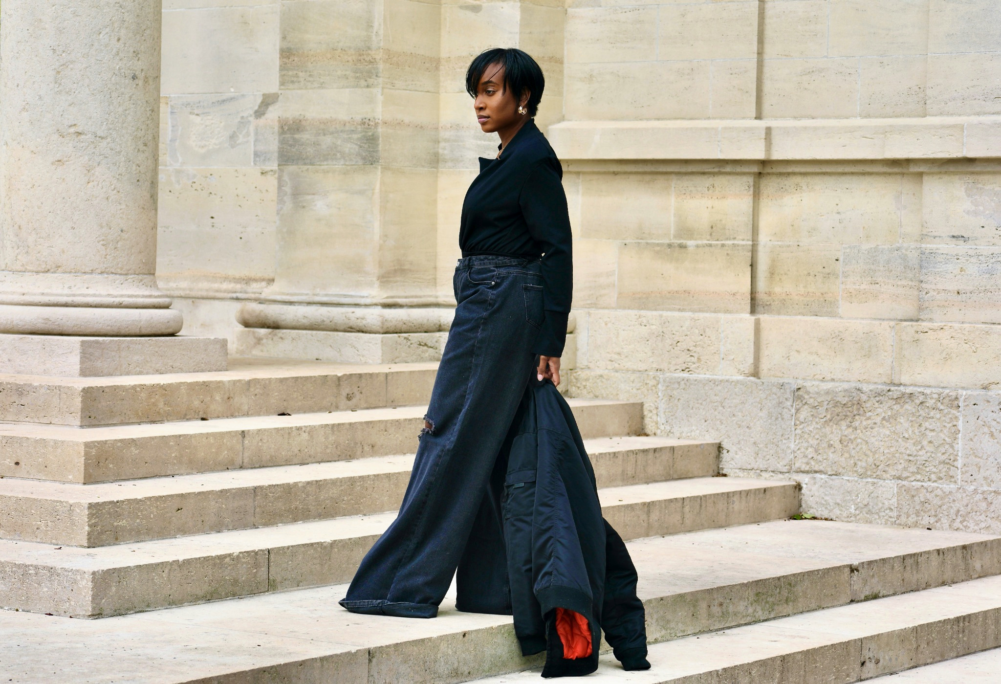 Tiffani Kennard walking through monumental stone architecture in black tailoring and wide-leg denim